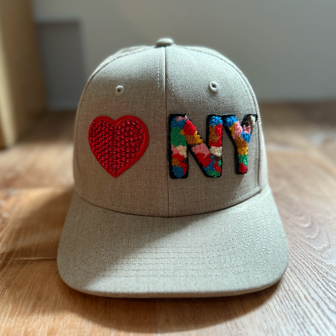 Beige cap with a red heart and colorful 'NY' on a wooden surface