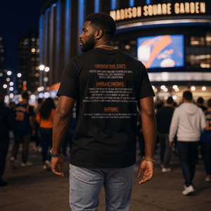A male model walking outside Madison Square Garden at night wearing the back of a black “Captain Clutch” Garbage Pail Ballers t-shirt featuring bold orange and white New York basketball inspired typography graphics. Cinematic NYC streetwear atmosphere with realistic crowd blur and luxury handmade urban fashion style by Rebel P Customs.